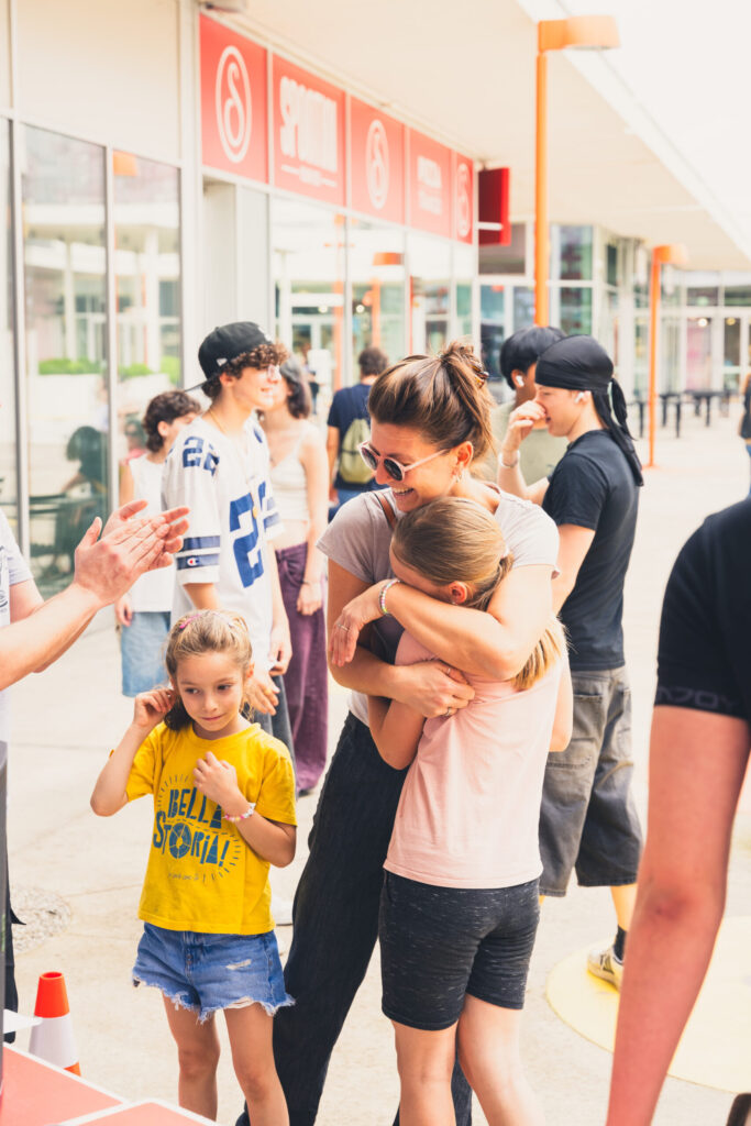 mamma e figlia che si abbracciano e intorno persone che si divertono e stanno insieme. questo e' il potere dello sport di strada, inclusione per donne e bambini