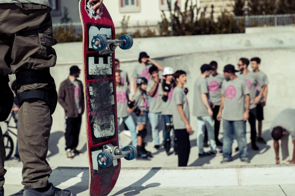 Ragazzo che tiene in mano uno skate. nello sfondo ci sono persone che condividono questa passione