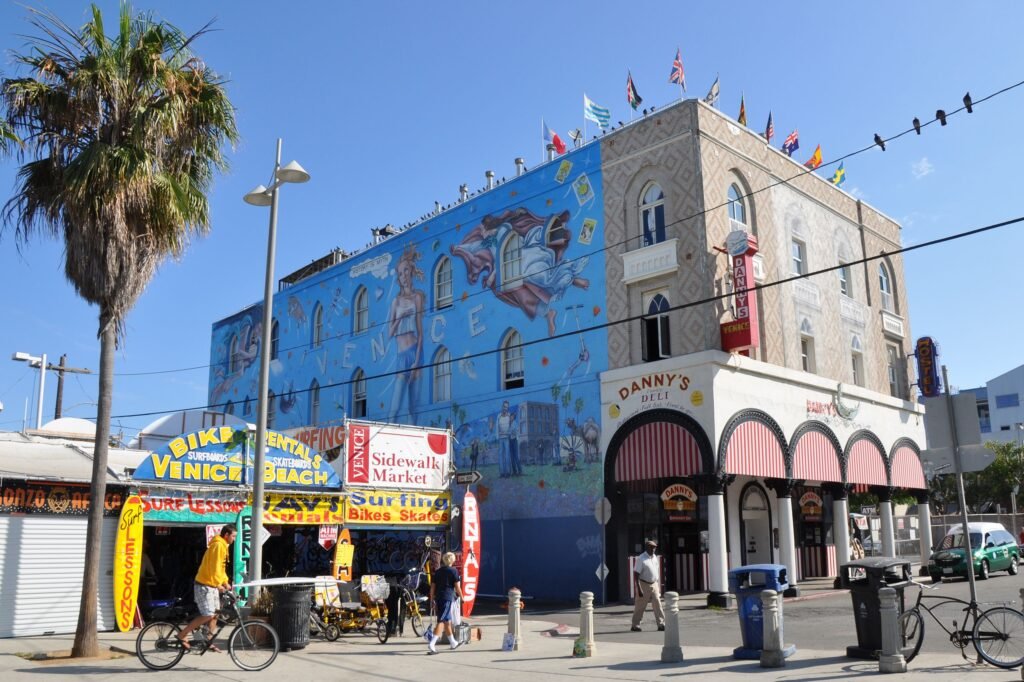 Strada a Venice Beach, Los Angeles in cui si vede un edificio con molte bandiere del mondo a rappresentare la multiculturalità. Sul lato di questo palazzo c'è un murales che raffigura Venere con lo stile pittorico italiano e dietro di lei la scritta Venice